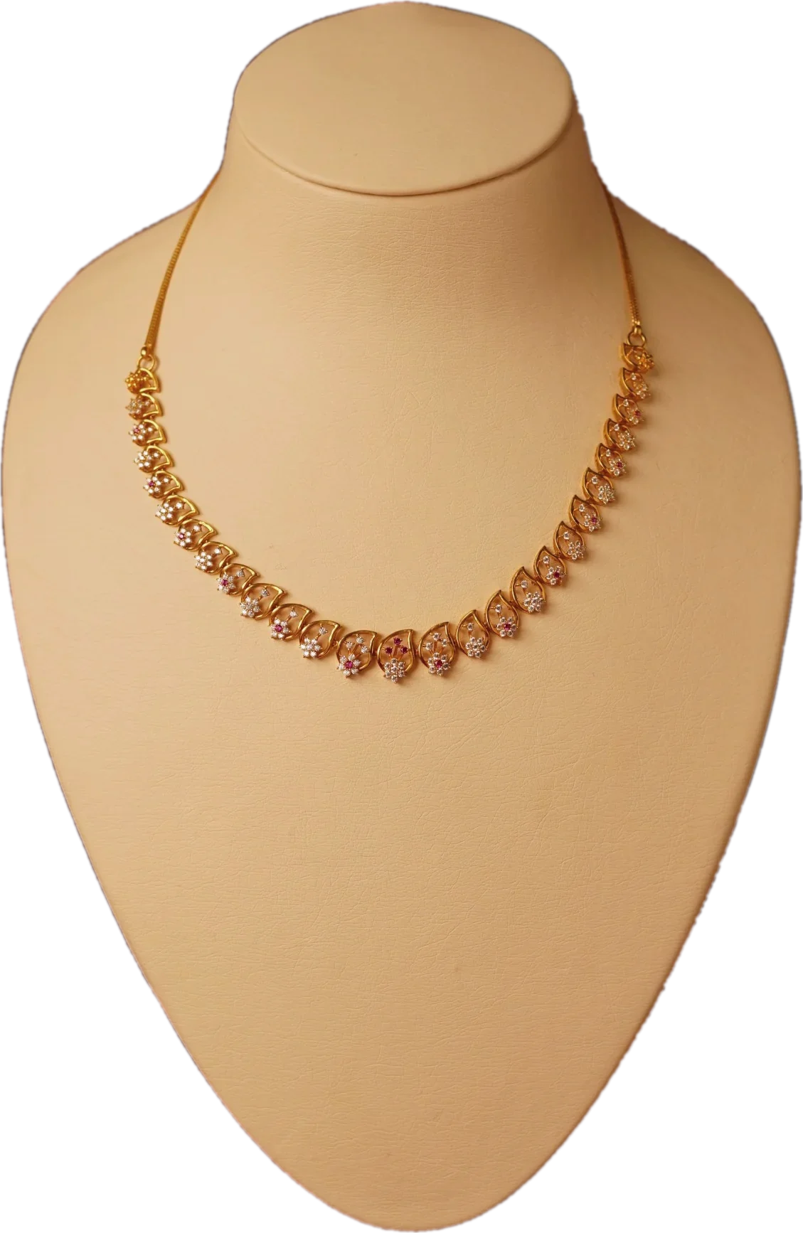 Gold necklace with diamond-set leaf links and small ruby accents on a cream display bust