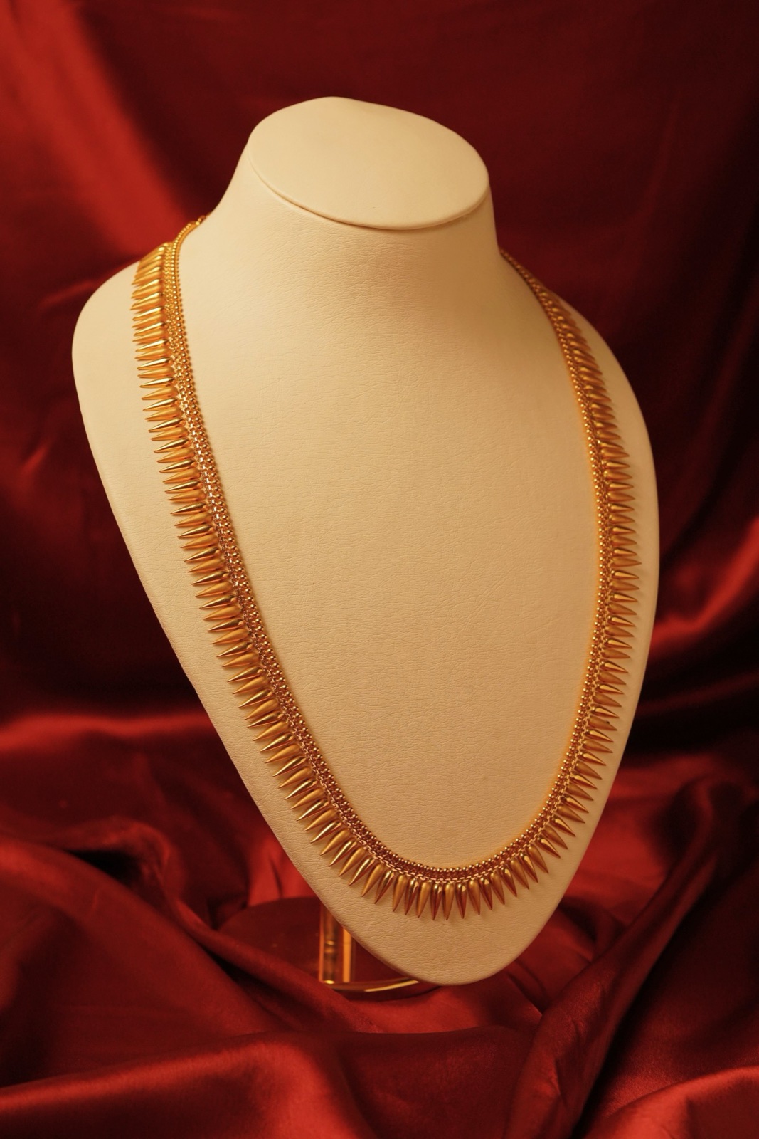 Long gold necklace with rows of spike-shaped drops on a display bust against red satin